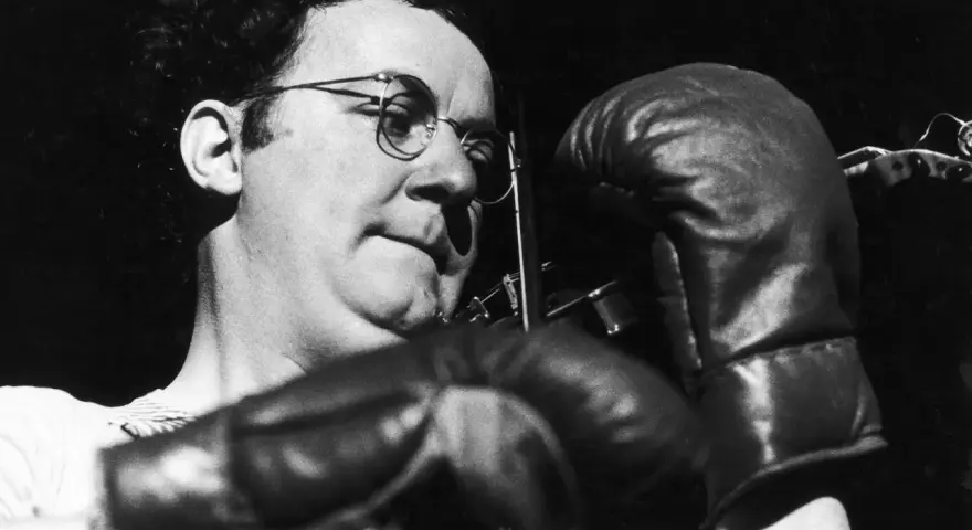 Coluche, lunettes rondes, gants de boxe, prêt à en découdre avec le racisme.
