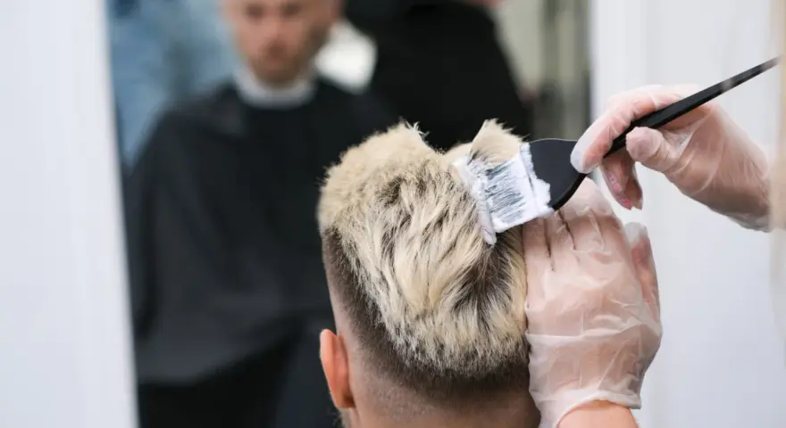 Fryzjer nakłada farbę na blond włosy mężczyzny.