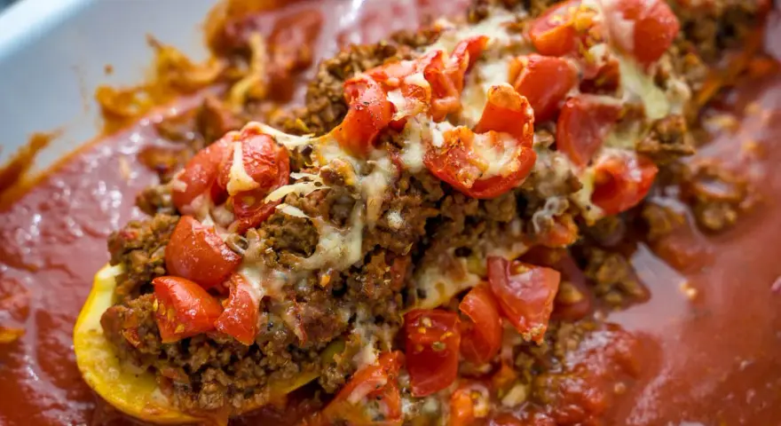 Herzhafte zucchini schiffchen gefüllt mit Hackfleisch, Tomaten und Käse, in einer aromatischen Tomatensauce.