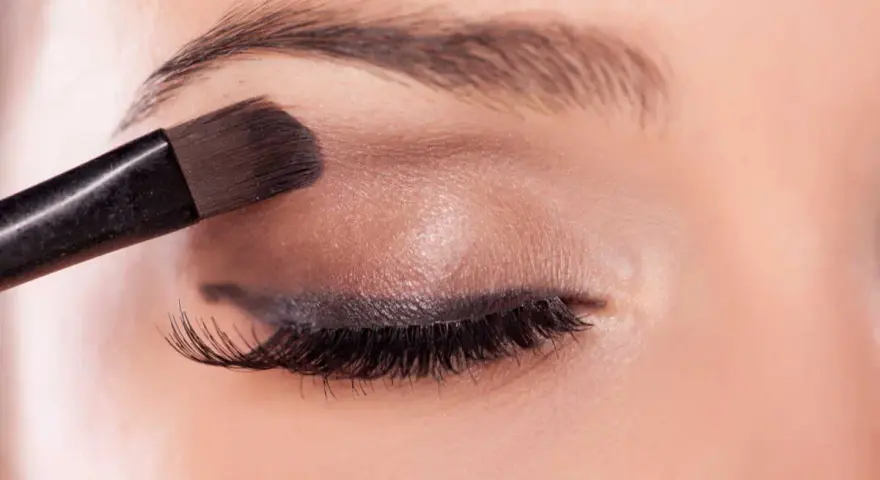 Application d'un fard à paupières marron pour un regard smoky intense.