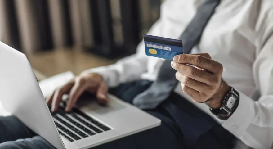 Mężczyzna w koszuli i krawacie trzyma kartę Visa Silver, gotowy do płatności online. Akcja pajacyk w tle.