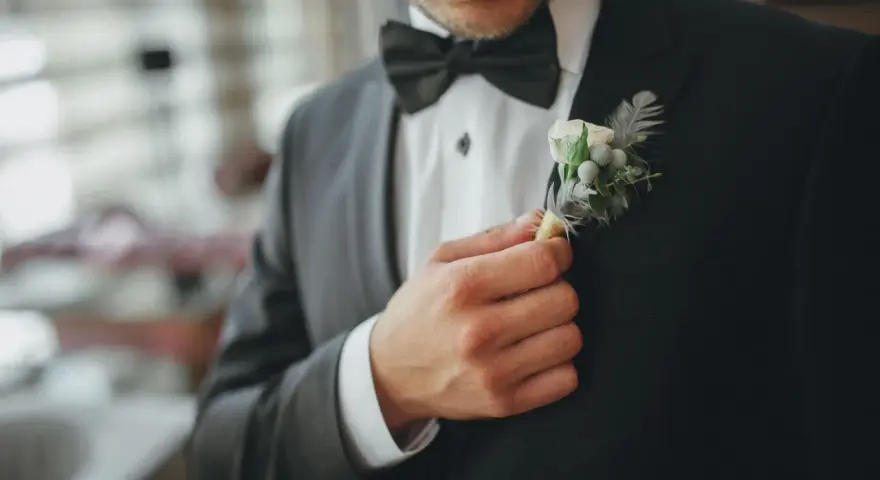 Mężczyzna poprawia butonierkę w eleganckim, czarnym garniturze.