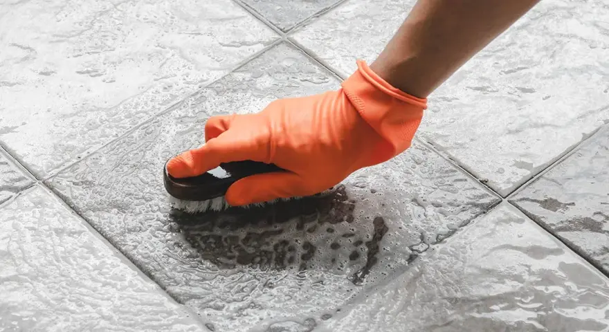 Mano con guanto arancione che strofina il pavimento del terrazzo con una spazzola, per togliere la ruggine e lo sporco.