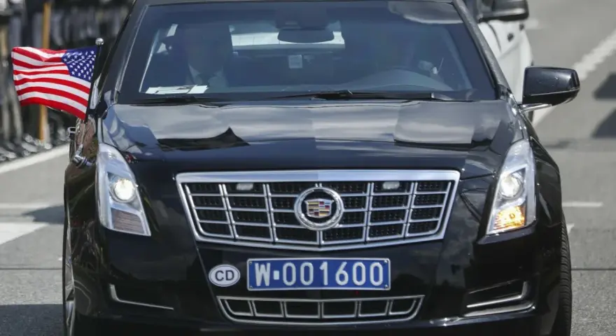 Czarny Cadillac z amerykańską flagą i tablicą rejestracyjną CD W-001600, wskazującą na rejestracje dyplomatyczne.
