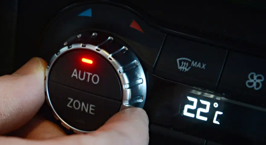 Hand dreht am Regler der **Klimaanlage Auto** auf 22 Grad Celsius. Rote LED leuchtet.