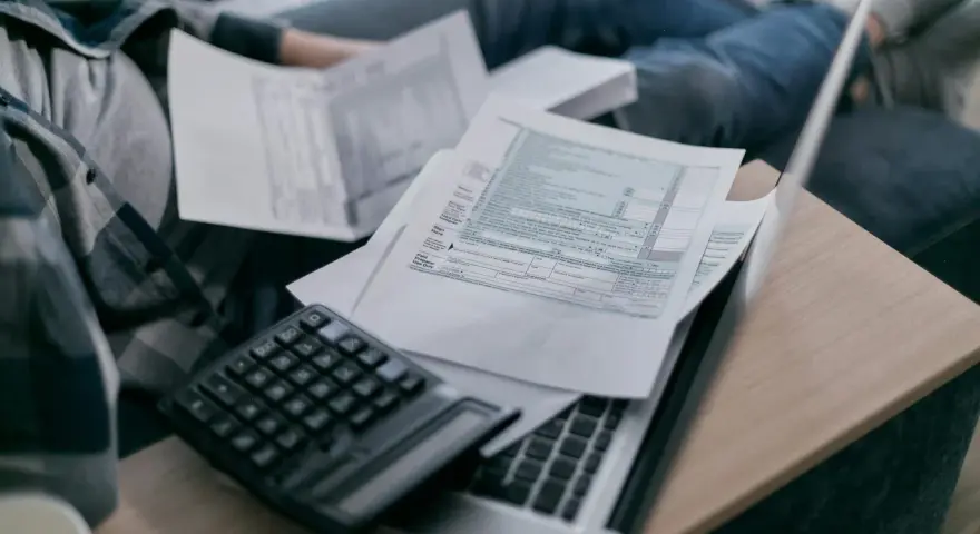 Osoba przegląda dokumenty podatkowe, kalkulator i laptop. Analiza składnik zmienny stawki sieciowej.