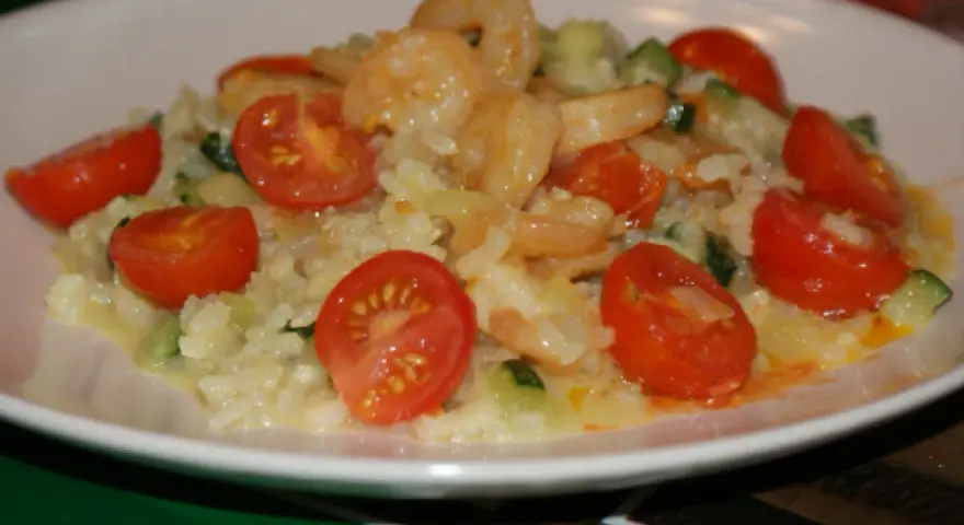 Risotto z krewetkami i pomidorkami koktajlowymi na białym talerzu.