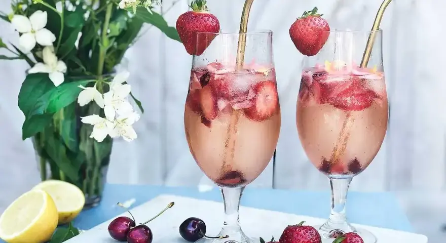 Två glas med ett uppfriskande drink med gin, fyllda med is, jordgubbar och körsbär. En perfekt sommardrink!
