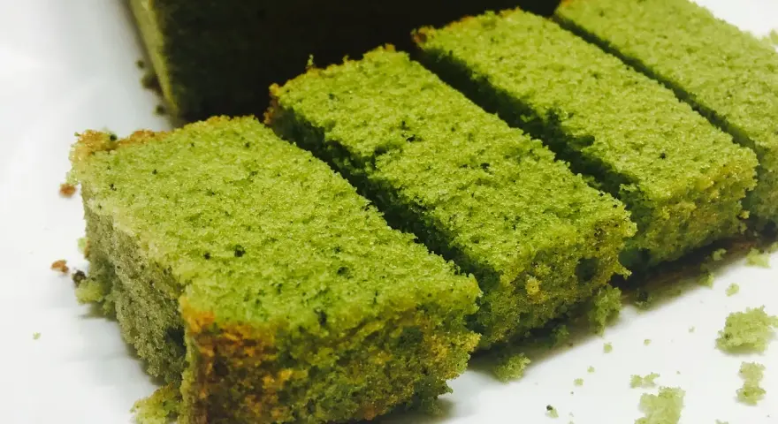 Puszyste ciasto matcha pokrojone w prostokątne kawałki, ułożone na białym talerzu.