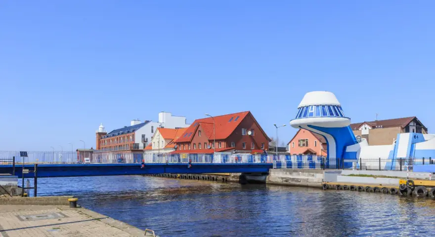 Port rybacki nad Wieprzą z niebieskim mostem i charakterystycznym budynkiem w kształcie statku kosmicznego.