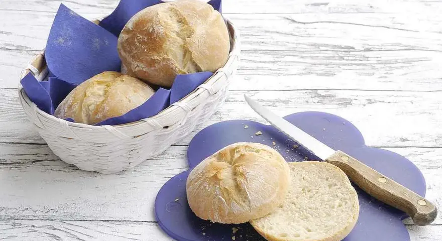 Frisch gebackenes, weiches Brot liegt in einem Korb und auf einem lila Brett. Ein Messer liegt daneben.