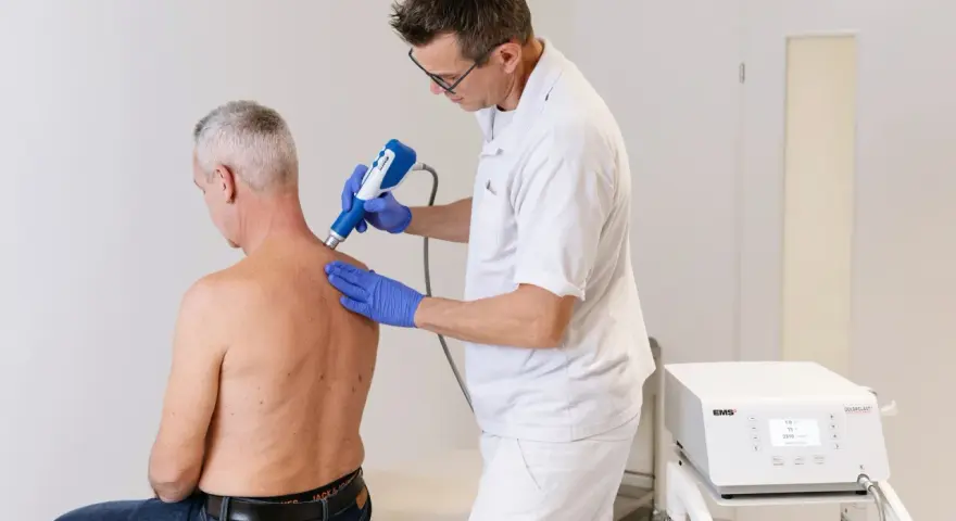 Therapeut behandelt Manns Schulter mit Stoßwellentherapiegerät. Es tut nicht weh, wie eine Spritze in die Schulter.