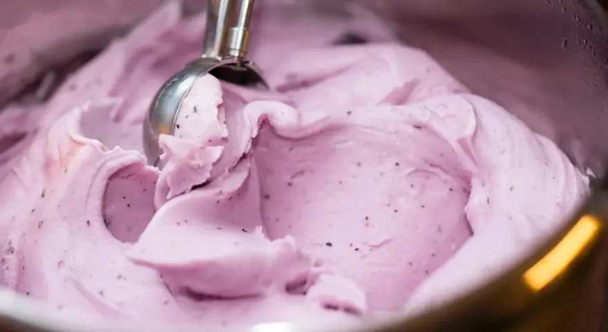 Ein Löffel nimmt eine Kugel cremiges, lila Beeren-Eis aus Milch.