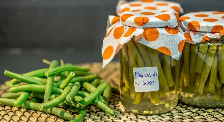 Fagiolini sott'olio in agrodolce, conservati in barattoli con tappi decorati. Freschi e pronti per essere gustati.