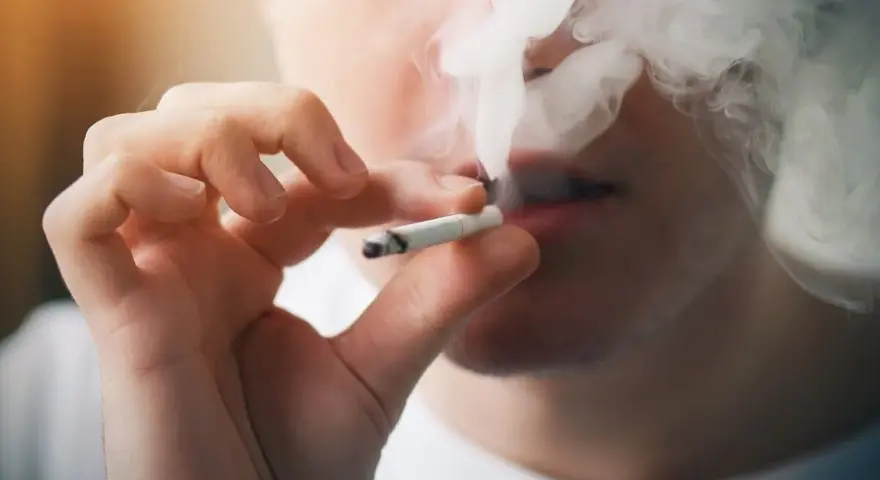 Persona fumando un cigarrillo, exhalando humo denso. Podría ser un indicio de sobredosis de nicotina.