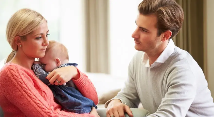 Zmartwiona mama tuli dziecko, a ojciec patrzy z troską. Czy to baby blues? Co to za uczucie?