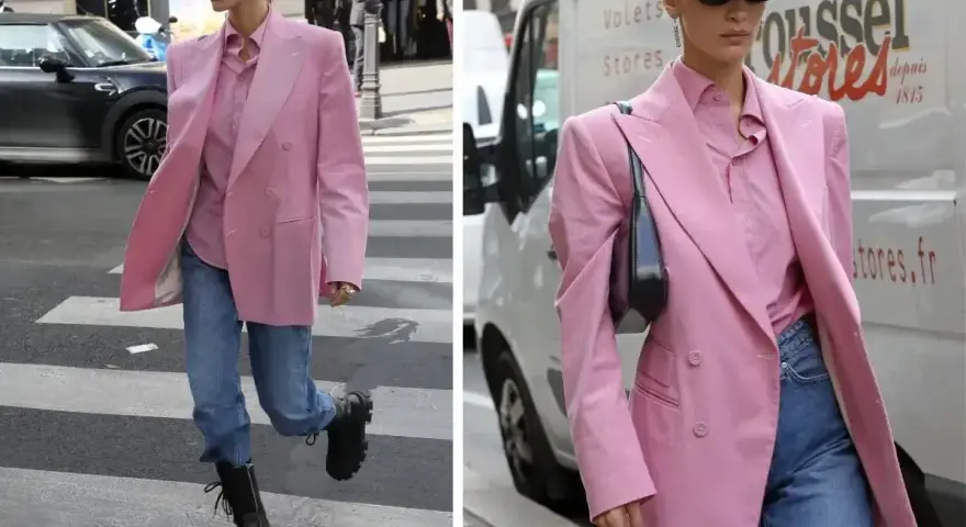 Kobieta w marynarce w odcieniu **magenta kolor** i jeansach idzie ulicą. Czapka z daszkiem i okulary dodają jej miejskiego stylu.