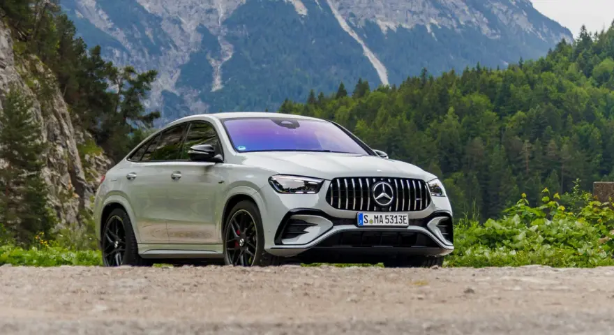 Biały Mercedes GLE 53 AMG coupe na tle górskiego krajobrazu z lasem.