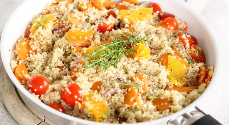 Salade de quinoa colorée avec carottes, tomates cerises et quartiers d'orange, garnie de thym. Un plat savoureux qui met en avant les quinoa bienfaits.