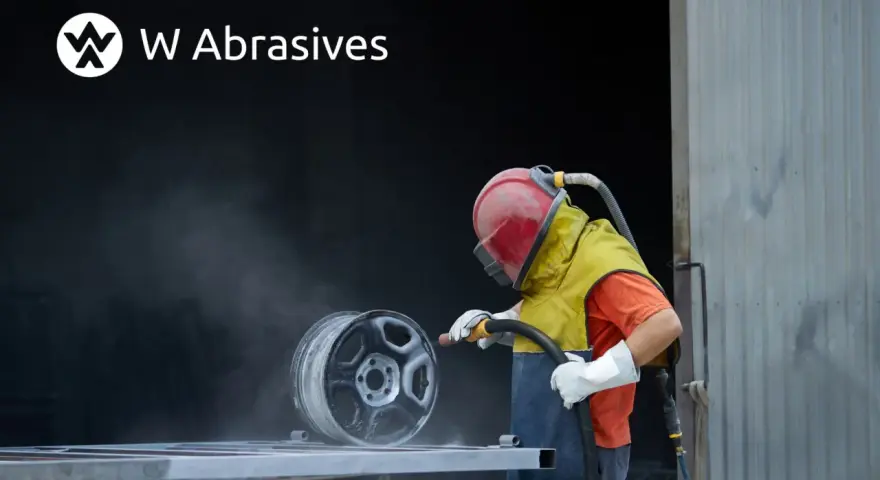 Pracownik w kasku i ochronnym ubraniu wykonuje piaskowanie aluminium felgi.