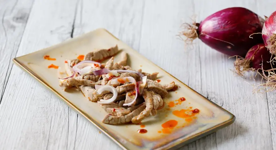 Straccetti di vitello conditi con cipolla rossa e un filo d'olio piccante, pronti per essere gustati.