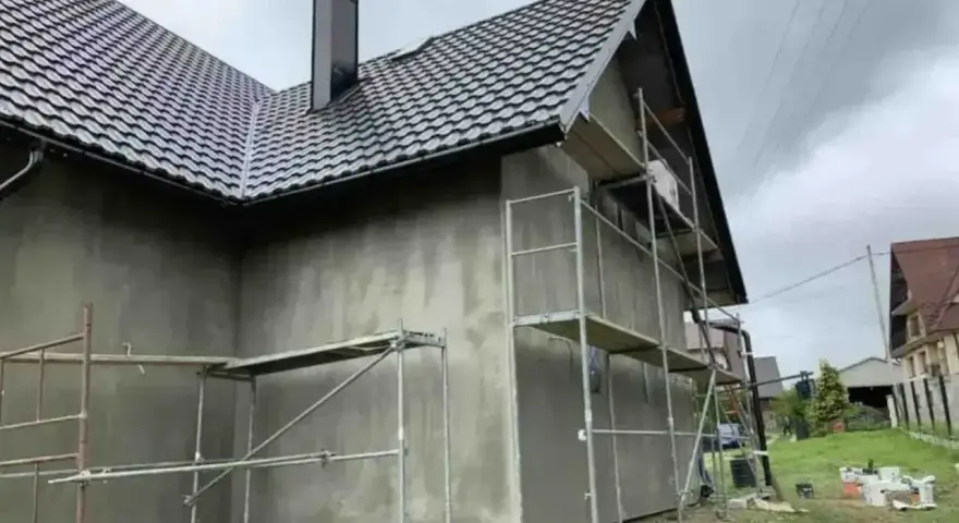 Dom w trakcie prac elewacyjnych. Widać rusztowania i szarą ścianę, która czeka na tynk silikonowy. Cena za m2 robocizny jest kluczowa dla budżetu.