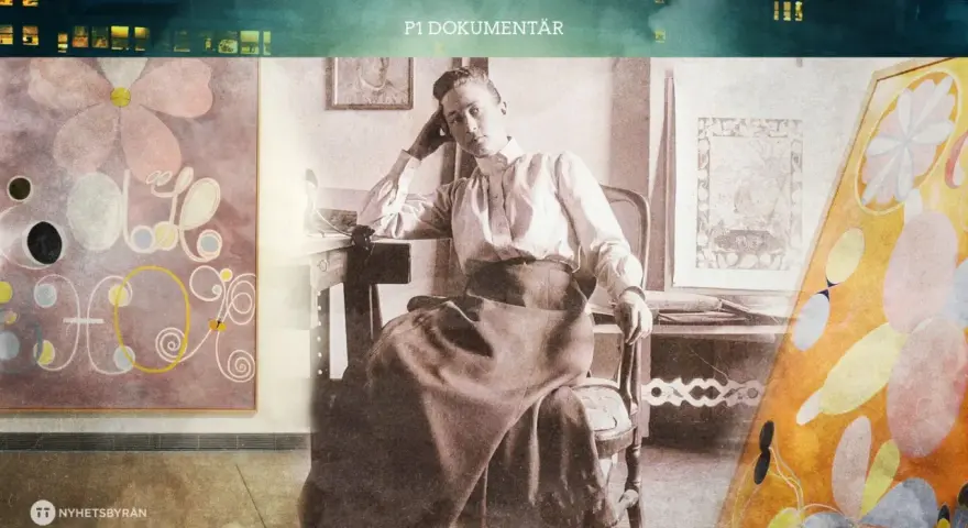 Hilma af Klint barn, en ung kvinna i en vit blus och mörk kjol, sitter vid ett bord omgiven av sina abstrakta målningar.