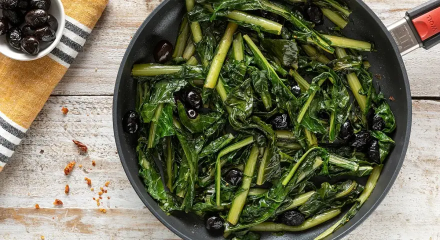 Verdura di catalogna saltata in padella con olive nere. Un piatto semplice e gustoso, pronto per essere servito.