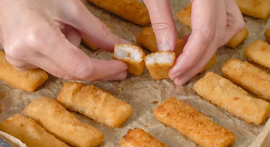 Ręce rozdzielają chrupiące paluszki rybne. Idealne na szybki obiad, warto sprawdzić paluszki rybne kcal.