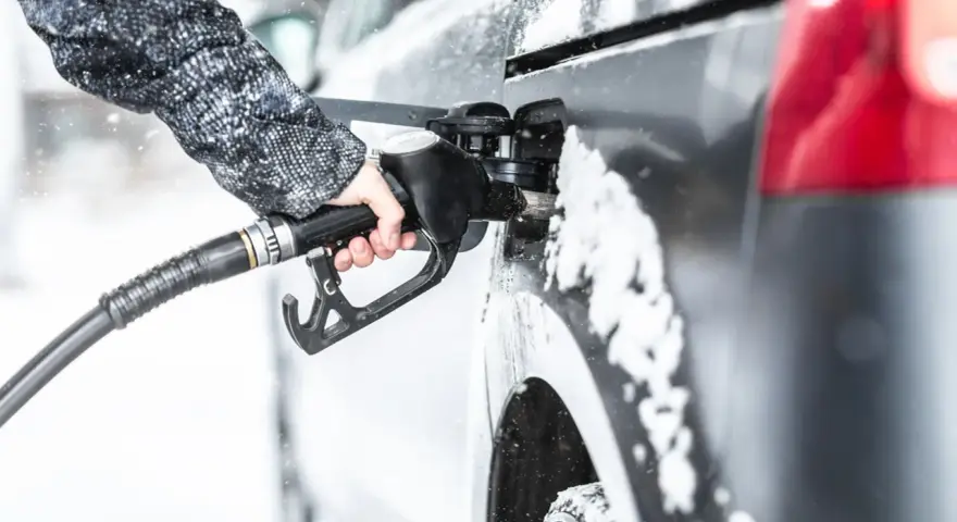 Ręka w zimowej kurtce trzyma pistolet do tankowania, nalewając diesel paliwo do samochodu podczas opadów śniegu.