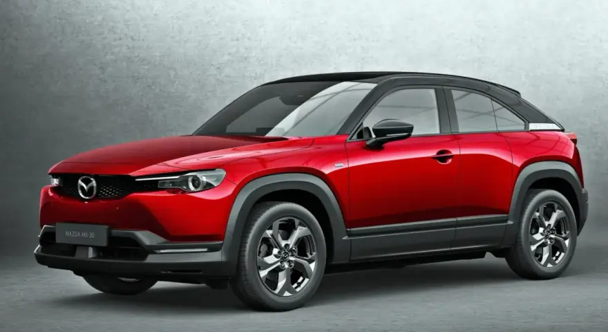 Czerwona Mazda MX-30 z czarnym dachem prezentuje się stylowo na tle szarej ściany.
