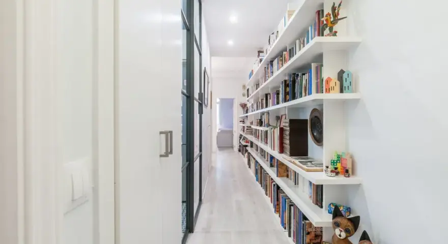 Pasillos estrechos y modernos con estanterías blancas repletas de libros y objetos decorativos, creando un ambiente acogedor.