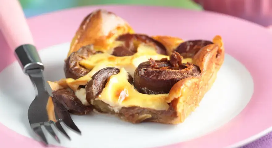Tranche de clafoutis aux prunes moelleux sur une assiette rose avec une fourchette.