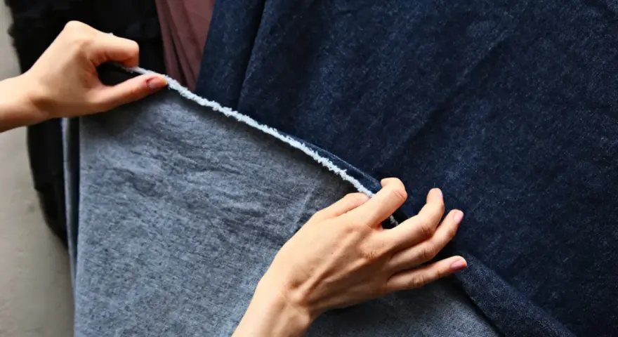 Dłonie dotykają ciemnoniebieskiego denimu i szarej tkaniny, być może z domieszką elastanu, sprawdzając ich fakturę.