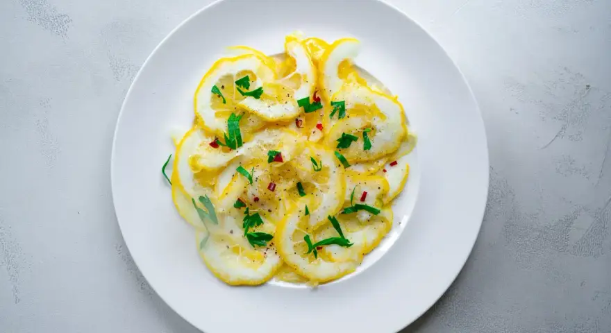 Dünne Scheiben Zitrone mit Zucker bestreut, garniert mit frischen Kräutern und Chiliflocken. Ein erfrischender Genuss!