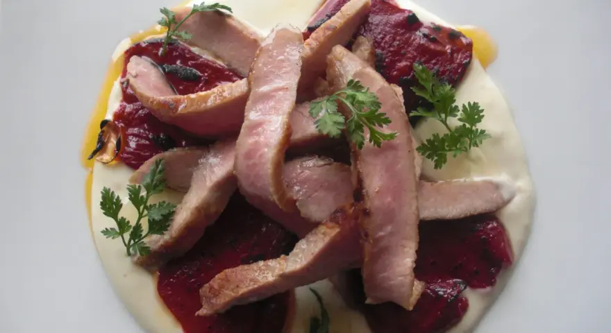 Lonchas de cerdo tierno sobre una cama de puré cremoso y pimiento del piquillo asado, decorado con perejil fresco.