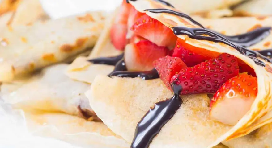 Deliziose crepes senza burro, ripiene di fragole fresche e ricoperte da una golosa salsa al cioccolato.