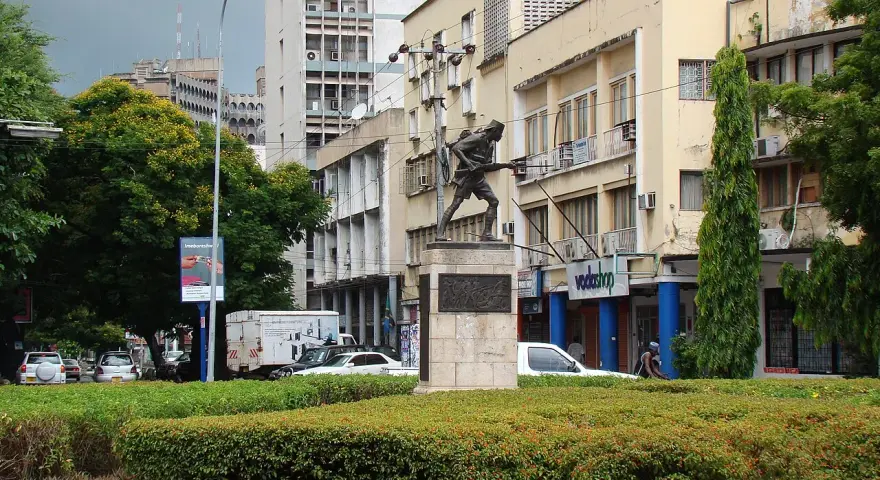 Pomnik żołnierza na tle budynków w Dar es Salaam. W tle widać ruch uliczny i drzewa.