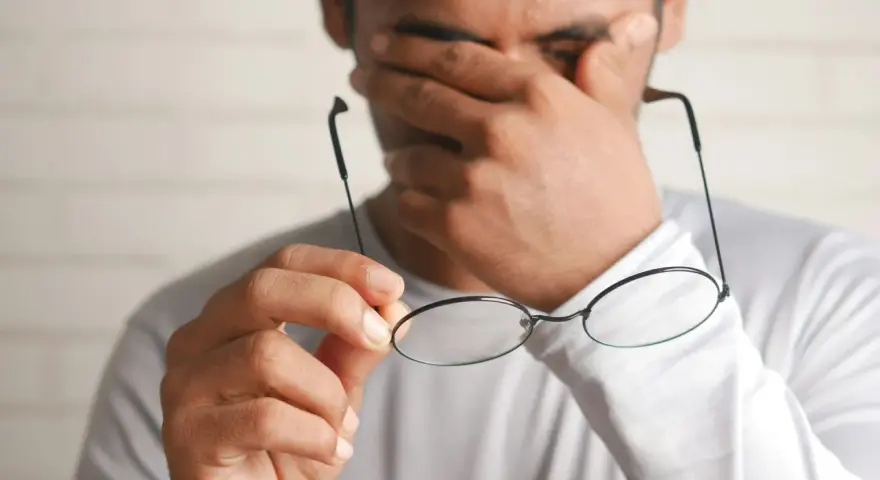 Zmęczony pracownik pociera oczy, trzymając okulary. Marzy o urlopie bezpłatnym zgodnie z kodeksem pracy.