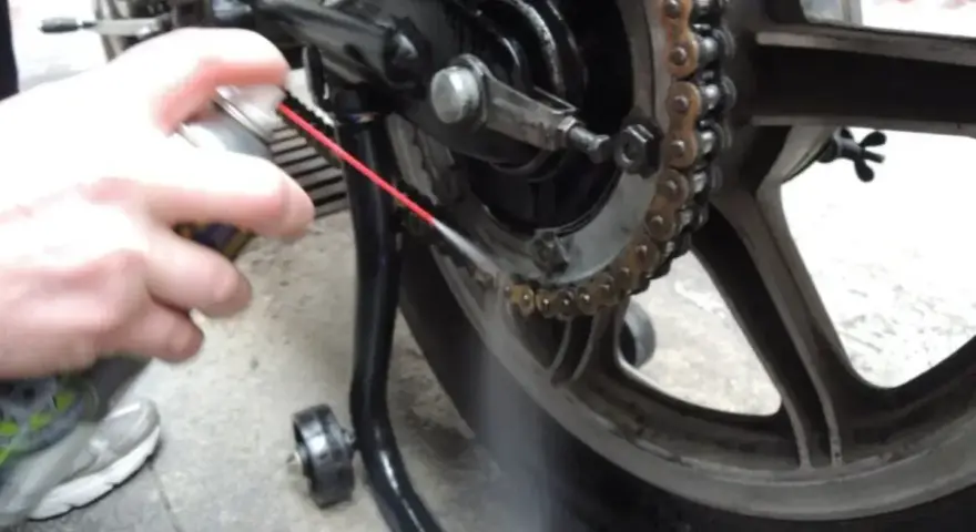 Mano spruzza lubrificante sulla catena della moto. Per sapere ogni quanto ingrassare catena moto, controlla il manuale.