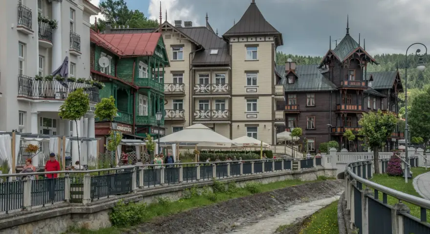 Krynica-Zdrój latem: malownicza promenada nad potokiem, zabytkowe wille i kawiarniane ogródki.