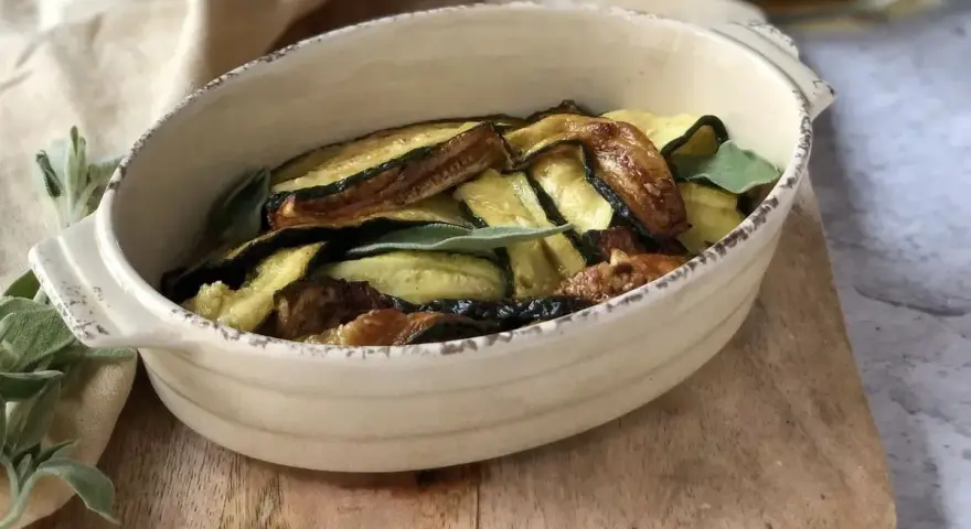 Zucchine in carpione dorate e saporite, guarnite con foglie di salvia fresca, servite in una ciotola rustica.