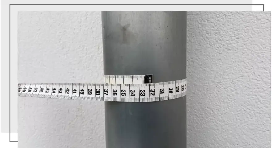 Miarka krawiecka owinięta wokół szarej rury pokazuje, jak zmierzyć średnicę rury. Odczyt wynosi około 32 cm.