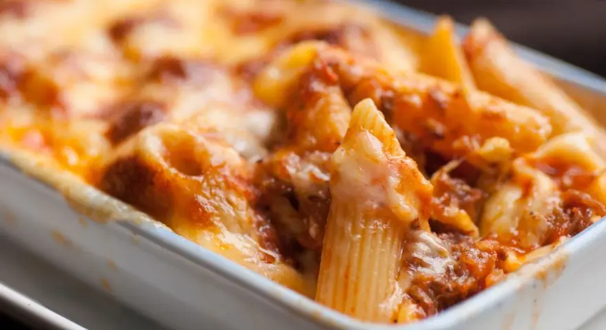 Un invitante piatto di pasta al forno, con penne ricoperte da un ricco sugo e formaggio filante, pronto per essere gustato.