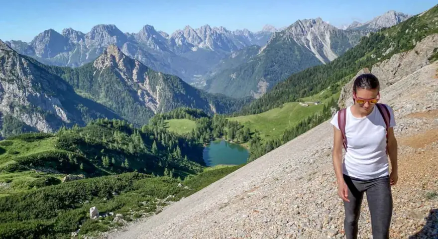 Una donna fa una camminata outdoor in montagna, godendosi il panorama di un lago alpino e vette maestose. Il vero significato di camminata outdoor è qui.