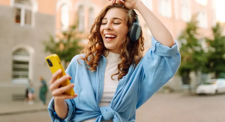 Kobieta w słuchawkach i niebieskiej koszuli trzyma żółty telefon, słuchając muzyki.