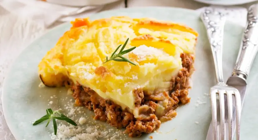 Pyszna zapiekanka pasterska (Shepherd's Pie) z warstwą mielonego mięsa i kremowym purée ziemniaczanym, ozdobiona gałązką rozmarynu.
