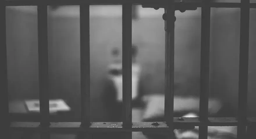 Widok przez kraty więzienne. Ciemne, ponure wnętrze celi, symbolizujące karę pozbawienia wolności.