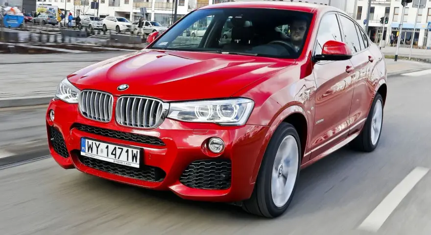 Czerwone BMW X4 w ruchu miejskim. Wady tego modelu mogą dotyczyć widoczności z tyłu i ograniczonej przestrzeni bagażowej.