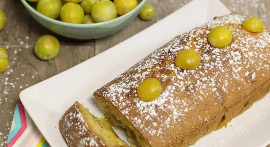 Gâteau lorrain aux mirabelles, saupoudré de sucre glace, avec des mirabelles fraîches sur le dessus et dans une coupelle à côté.